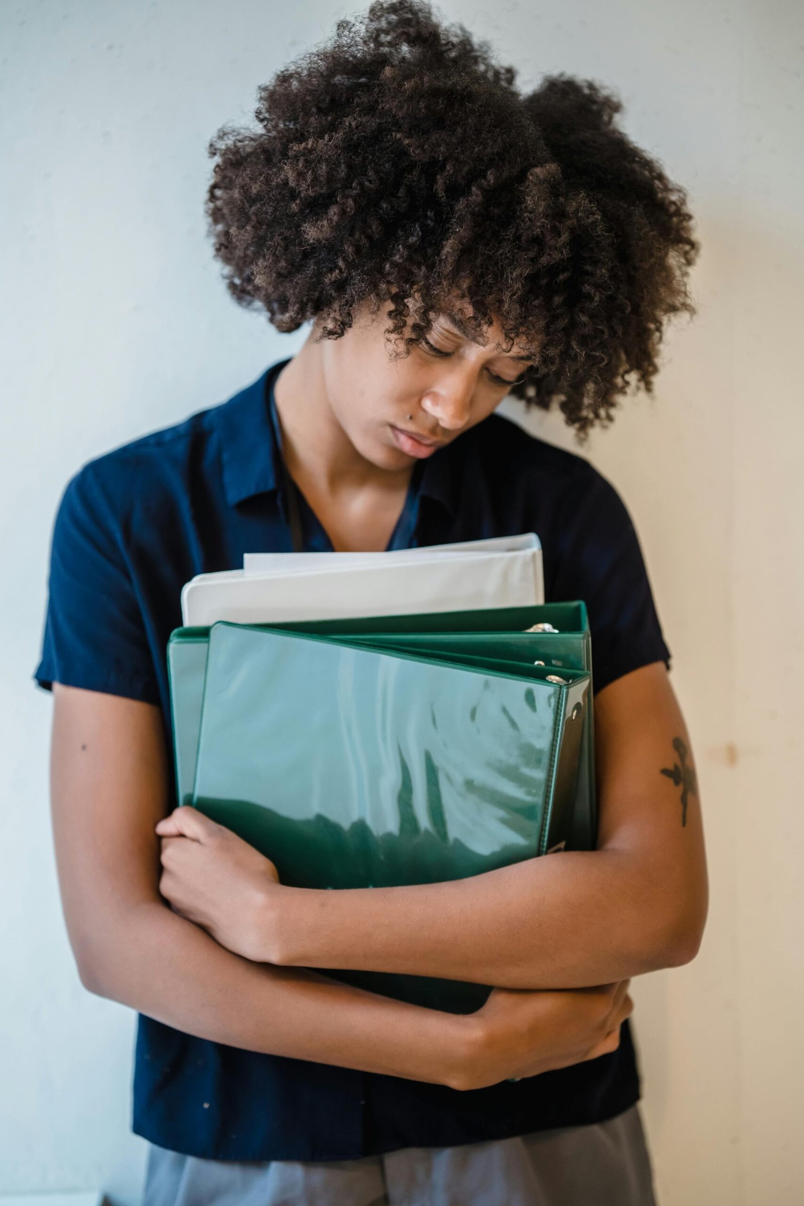 Young African American woman in an office holding binders, expressing a busy workday mood.