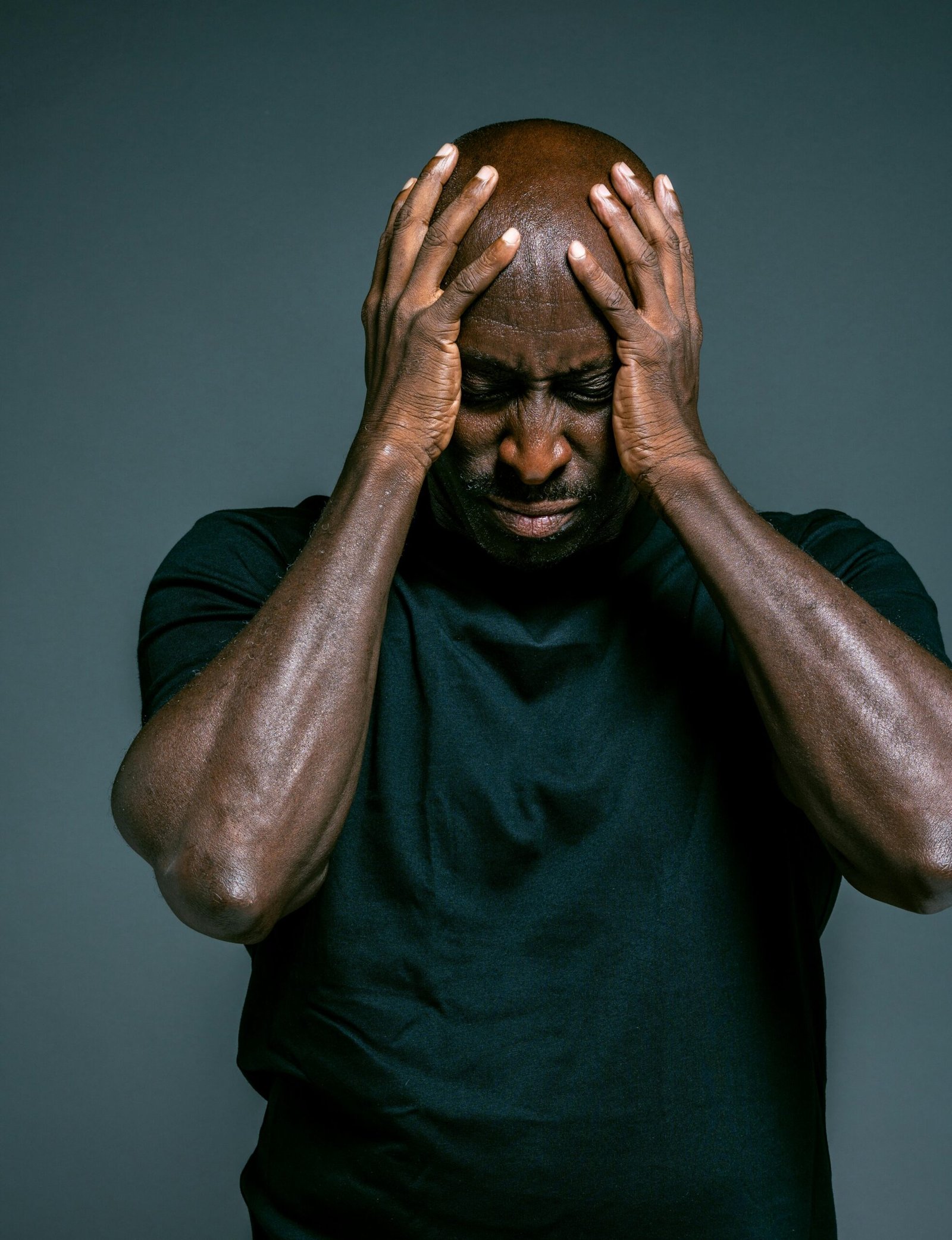 Portrait of a stressed man with a pained expression, hands on head, wearing a black shirt.